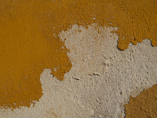 Close-up of a weathered wall with peeling ochre paint, revealing rough beige plaster underneath. Aged surface texture ideal for backgrounds or design overlays