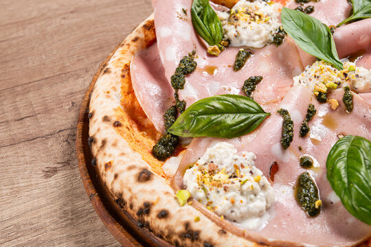 A close-up of a delicious Italian pizza featuring mortadella slices, ricotta cheese, basil leaves, pesto sauce,