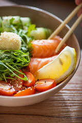 A healthy poke bowl served with fresh salmon slices, cucumber ribbons, arugula, avocado, cherry tomatoes