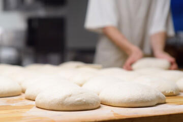 A batch of formed dough pieces on a table in the kitchen of a local bakery ready to bake. Olive ciabatta blanks laid out in a row in front of a large oven. Local bread production