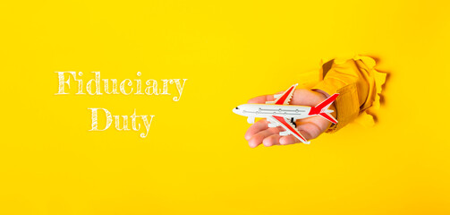 Obraz premium Hand holding a toy airplane with the words Fiduciary Duty written below it