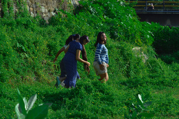 Fototapeta premium Laughing and playful, the girls run together among thick grass and flowering plants.