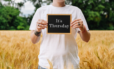 Man holding a chalkboard with the words Its Thursday written on it