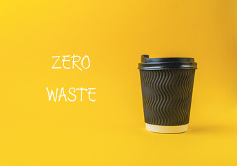 Black coffee cup with a white lid sits on a yellow background
