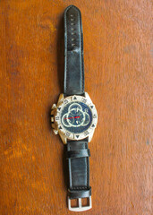 Luxury analog wristwatch with a black leather strap and stainless steel bezel, placed on a wooden surface, showcasing bold numerals and a modern chronograph dial.
