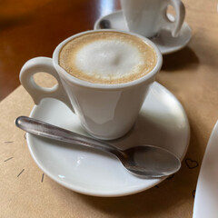A classic extended espresso with milk, served in a elegant white cup on a matching saucer with a spoon. The creamy texture of the milk and the rich color of the coffee are highlighted.