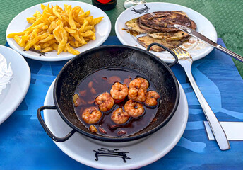 sizzling spicy prawns (gambas pil pil) cooked in a flavorful garlic and chili oil, served in a rustic ceramic dish. The steam rising from the dish adds to the inviting and delicious appeal.