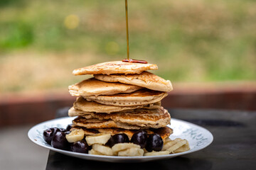 A stack of fluffy pancakes, drizzled with syrup and accompanied by sliced bananas and cherries.