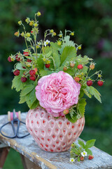 Blumenstrauß mit pink Rose und Erdbeeren in einer Vase im Garten