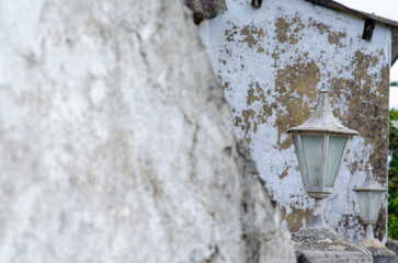 Aged outdoor lantern with faded glass stands against an old, textured, weathered plaster wall,...