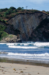 Dramatic rocky cliff rises above crashing ocean surf and a tranquil sandy shore, showcasing the raw beauty of coastal nature. Ideal for nature and travel concepts.