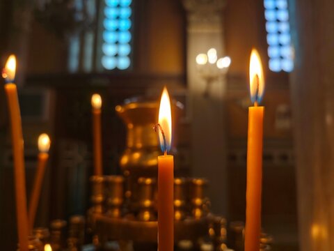 Closeup view of lit Orthodox prayer candles in a brass holder inside a dimly lit church, casting a warm, serene glow and creating a peaceful, spiritual atmosphere.