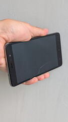 A hand is shown gripping a smartphone with a cracked screen