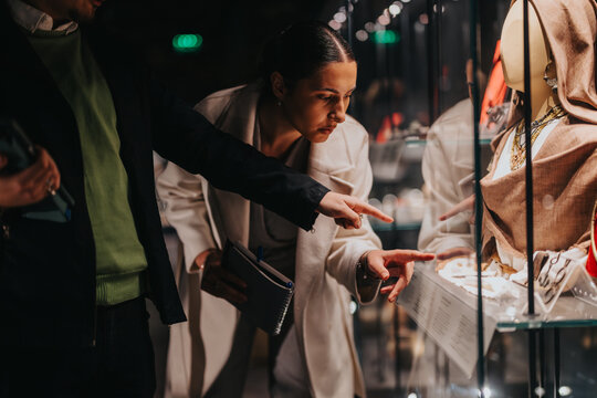 Two people examining artifacts displayed in a museum exhibit case, conveying curiosity and exploration in a cultural or educational setting.