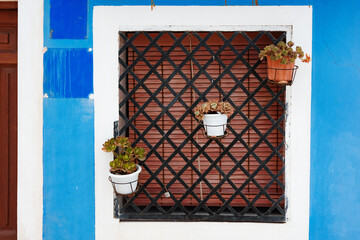 Window with iron grille and hanging flower pots on a bright blue wall. Concept of mediterranean...