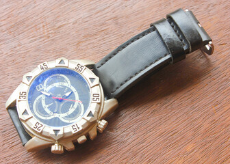 Luxury analog wristwatch with a black leather strap and stainless steel bezel, placed on a wooden surface, showcasing bold numerals and a modern chronograph dial.
