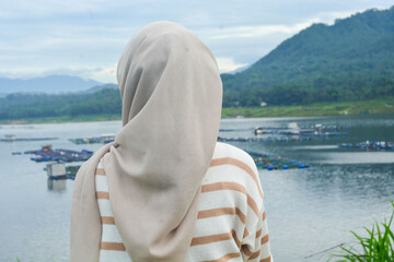 A female fish farm manager wears a safety vest and carries a book to check the work.