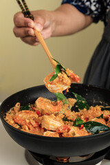 Female Hand Cooking Shrimp with Salted Egg Sauce using Long Chopstick on Black Pan