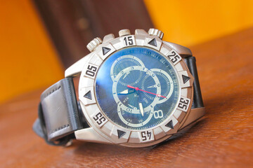 Luxury analog wristwatch with a black leather strap and stainless steel bezel, placed on a wooden...
