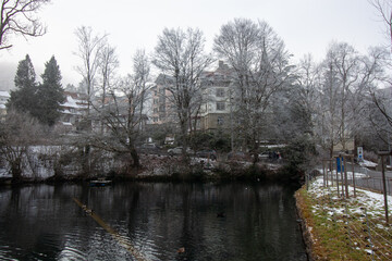 A serene winter landscape in St. Gallen, showcasing a tranquil body of water reflecting the bare...