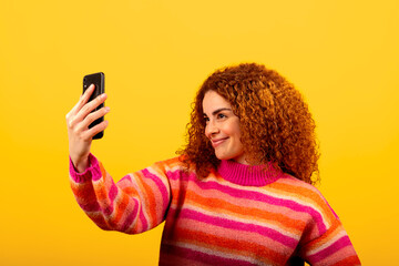 Young woman taking a selfie with smartphone smiling on yellow background