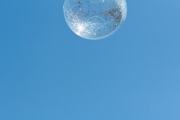 Floating soap bubble illuminated by sunlight against a clear blue sky during daytime