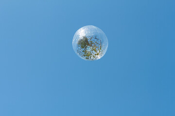 Beautiful soap bubble floating in a clear blue sky with reflections of nature during a sunny day