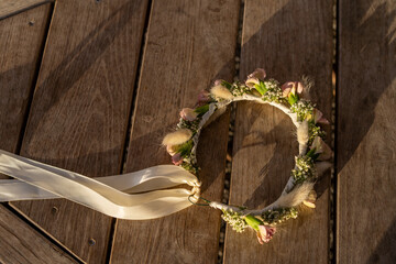 A handcrafted floral crown adorned with roses, gypsophila, and wheat rests on wooden table. Its elegant simplicity enhances the festive atmosphere of Shavuot, Wedding, Birthday and engages with nature
