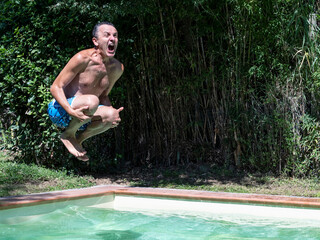 A man dives into the pool screaming, with bamboo plants nearby