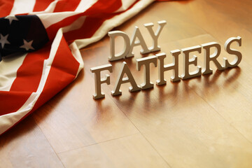 Wooden Letters Spelling 'Fathers Day' With American Flag Draped in Background on Wooden Surface
