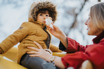 A heartwarming scene of a mother taking care of her child, dressed in cozy winter clothing, in an...