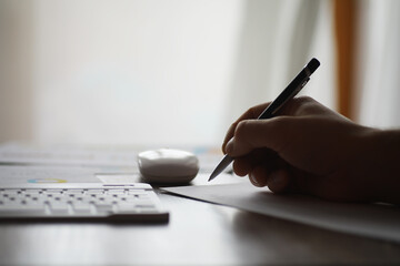 Person Writing on Paper with Pen at Desk Beside Computer Keyboard in Office