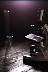 Microscope and Laboratory Glassware on Wooden Table in Dim Lighting for Scientific Research