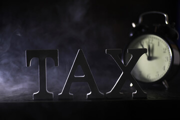 Time for Taxes Concept - Metal TAX Letters with Analog Clock in Dark Smoky Background