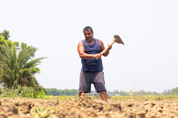 A farmer digs into the earth with steady focus, using a hoe to till the dry soil under the heat of the sun in a rural field