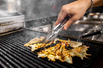 Close-up of a hand using tongs to grill shrimp on a barbecue. The shrimp are sizzling with steam rising, showcasing outdoor cooking with appetizing seafood