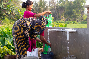 Mother and daughter fill green plastic bottles at a rural water tap