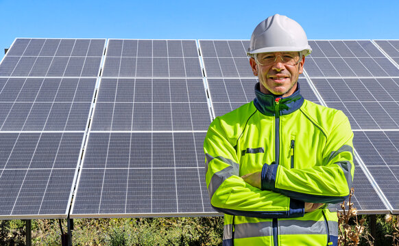 Technician or engineer with crossed arms and PPE at a solar panel installation for renewable photovoltaic energy.