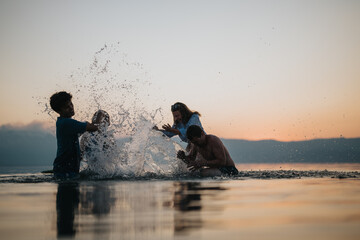 A group of friends enjoys splashing water on each other in a scenic lake at sunset. The vivid...