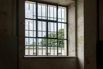Fototapeta premium Window with bars overlooking a historic building surrounded by trees on a cloudy day
