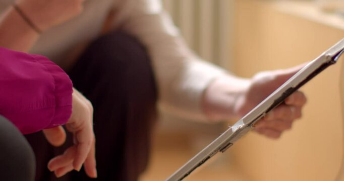 Two people share ideas on a tablet, pointing at the screen and engaging in a lively conversation. The closeup of their hands highlights the connection technology fosters in collaboration