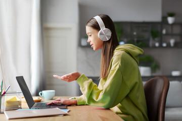 Digital learning. Teen girl video calling via laptop webcam during virtual lesson, engaging in e-learning online studies at home, side view