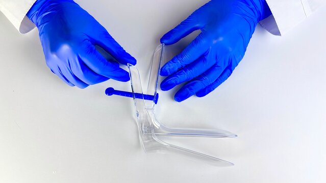 Doctor wearing blue gloves demonstrating the use of a clear plastic speculum on a laboratory table. Essential tool in gynecological examinations for safe healthcare practices