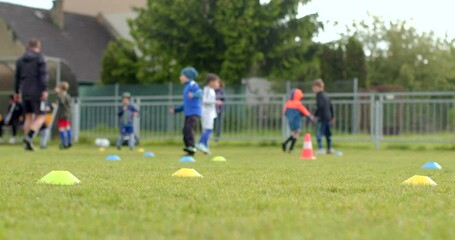Children are enthusiastically practicing soccer on a lush green field, with colorful cones set up for drills to enhance their skills, fostering a fun and healthy environment - Powered by Adobe