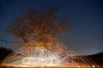 Nice night landscape with a lonely tree in the background of the stars. Long exposure shooting and fire show. Alternative landscape