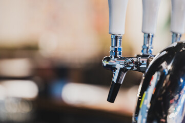 A close-up of a polished chrome beer tap with white handles in a bar setting. The blurred background enhances the sleek design, making it a perfect image for beverage-related themes