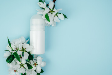 Deodorant bottles and flowers on blue background. Personal care product. Cleanliness and freshness