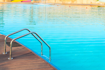 Steel chrome handrails of the swimming pool ladder with clear azure water