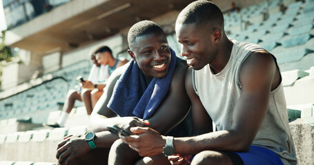 Sports, stadium and athlete friends with phone, smile and checking online schedule at team practice together. Relax, smartphone and men in bleachers for fitness app, progress tracking or workout plan © EinFrame25/peopleimages.com