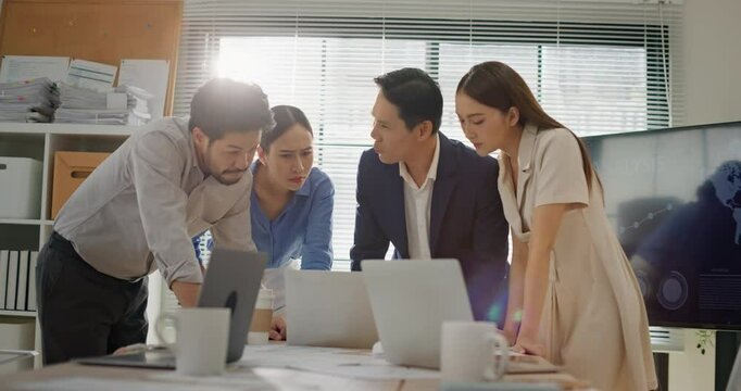 Multicultural business team gathered around laptop in modern office, focused on analyzing data, reviewing project strategy, collaborating on decision making with professional teamwork. Dolly zoom in.